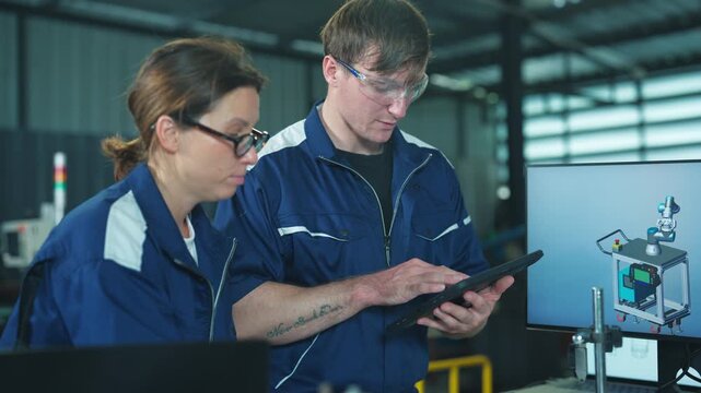 Industrial man and woman engineers discussing automated machinery plans. Using a laptop to monitor system control and factory efficiency.