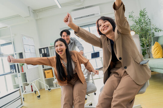 Three coworkers cheer triumphantly with raised fists, captured in a dynamic low angle in a bright office &mdash; an energetic celebration of team success, achievement, and workplace victory.