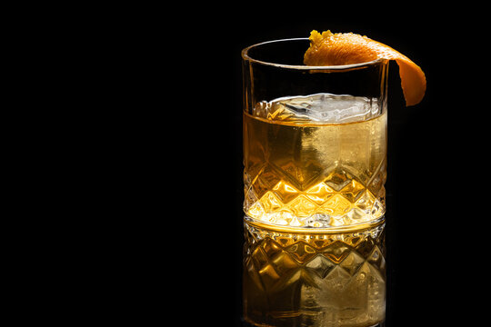 Close up of a classic old fashioned cocktail on a dark reflective background garnished with an orange twist.
