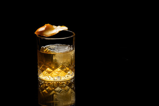 Close up of a classic old fashioned cocktail on a dark reflective background garnished with an orange twist.