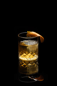 Close up of a classic old fashioned cocktail on a dark reflective background garnished with an orange twist.