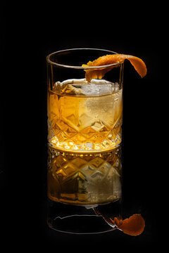 Close up of a classic old fashioned cocktail on a dark reflective background garnished with an orange twist.
