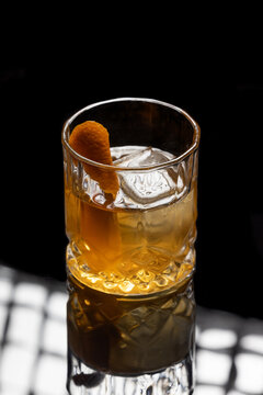 Close up of a classic old fashioned cocktail on a dark reflective background garnished with an orange twist.