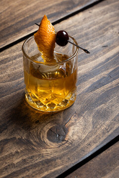 Close up of a classic old fashioned cocktail on a wooden background garnished with an orange twist and a cherry.