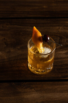 Close up of a classic old fashioned cocktail on a wooden background garnished with an orange twist and a cherry.