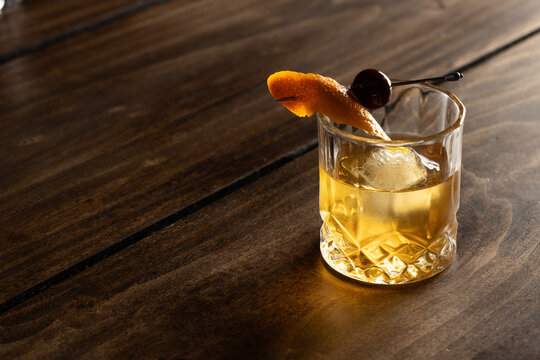 Close up of a classic old fashioned cocktail on a wooden background garnished with an orange twist and a cherry.