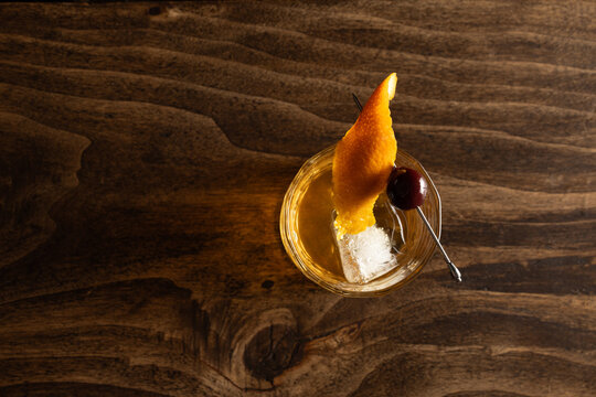 Close up of a classic old fashioned cocktail on a wooden background garnished with an orange twist and a cherry.