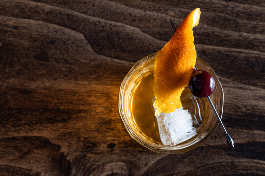 Close up of a classic old fashioned cocktail on a wooden background garnished with an orange twist and a cherry.
