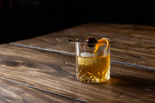 Close up of a classic old fashioned cocktail on a wooden background garnished with an orange twist and a cherry.