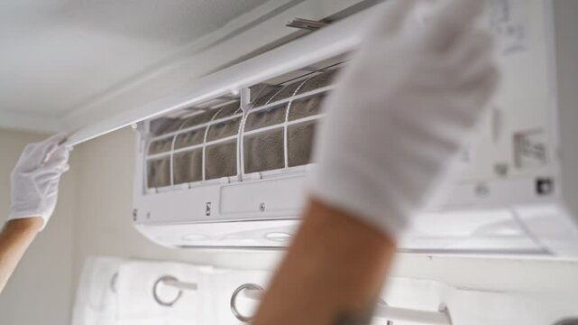 Close-up of gloved technician hands opening an air conditioner and inspecting dusty filters. HVAC maintenance, AC cleaning, professional servicing and appliance care concept.