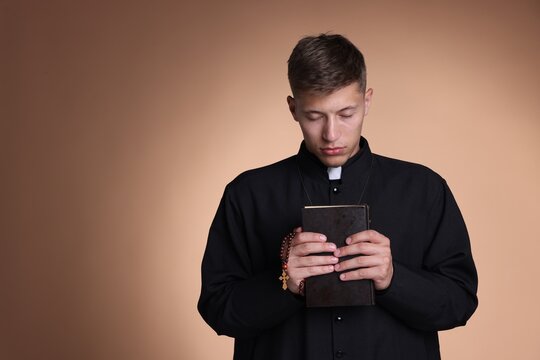 Priest with rosary and Holy Bible praying on beige background. Space for text