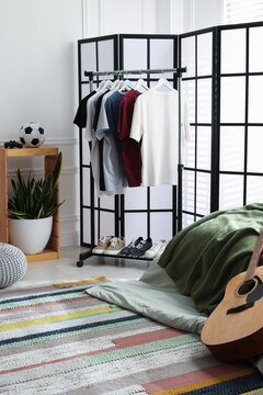 Teenager's room with folding screen, bed, guitar and clothes. Interior design