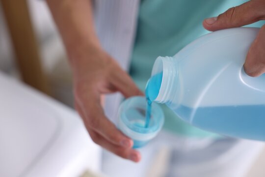 Man pouring liquid laundry detergent from bottle into cap, closeup