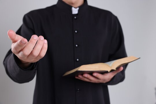 Priest with Holy Bible on grey background, closeup