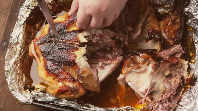 A woman's hands, using a sharp knife, cut a whole turkey baked with a spiced crust on foil. Medium shot.
