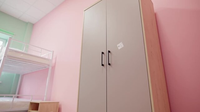 Bunk bed with clean mattress sits beside small wooden nightstand in dorm room. Modern furniture design ensures cozy living environment