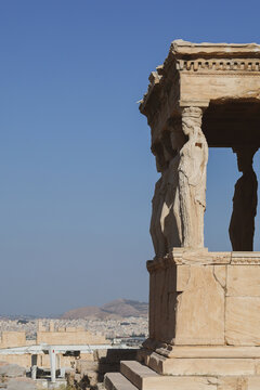 Marble Caryatid statues stand gracefully beneath the Erechtheion&rsquo;s porch on the Acropolis of Athens, illuminated by clear sunlight against a vivid blue sky overlooking the ancient city.