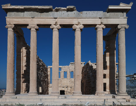 Front view of the Erechtheion temple on the Acropolis of Athens, displaying tall Ionic columns and weathered marble walls under a deep blue sky in bright afternoon light.
