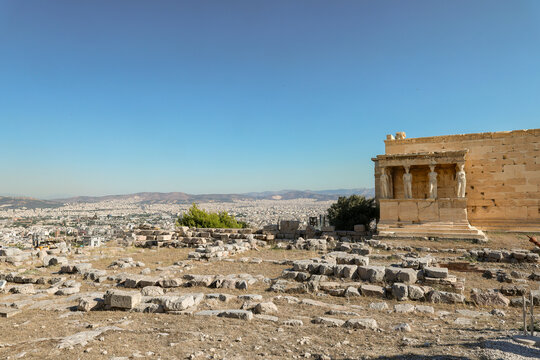 Wide view of the Acropolis of Athens showing the Erechtheion temple and surrounding ruins under a clear blue sky, overlooking the sprawling city and distant hills.