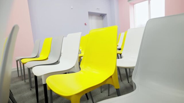 Plastic chairs with thin metal legs stand on soft carpet. Bright color palette enhances contemporary interior styling of presentation hall