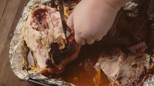 A woman's hands, using a sharp knife, cut a whole turkey baked with a spiced crust on foil. Medium shot.