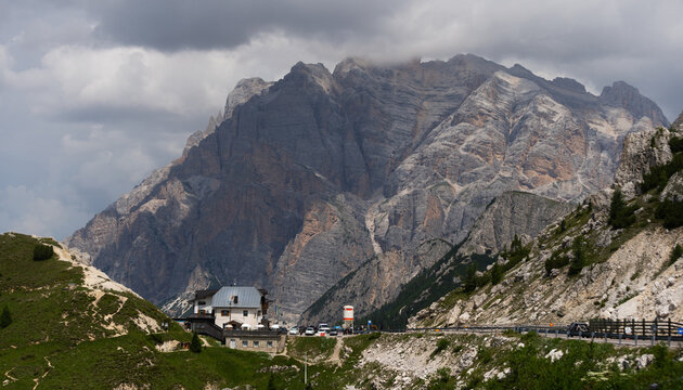 serene alpine valley with majestic mountain landscape and building in the background, viewed from a higher vantage point with gray, green, brown, and white colors.