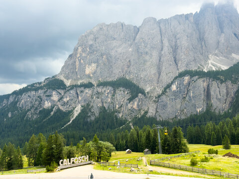 cable car ascending mountain landscape in alpine valley with forested slopes and rocky peaks, scenic and adventurous view from low angle, signboard reading 'calfosch' visible.