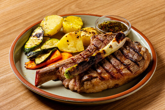 Juicy Grilled Ribeye Cowboy Steak Served with Roasted Potatoes, Grilled Zucchini, Carrots, and Chimichurri Sauce