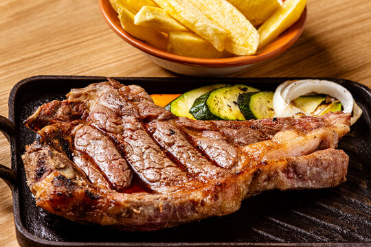 Grilled Ribeye Bone-In Steak Served on Cast Iron Skillet with French Fries, Grilled Vegetables, and Chimichurri Sauce
