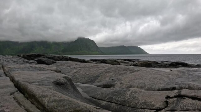 Static ultra wide view of smooth granite rocks and misty ocean mountains in Senja Norway