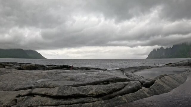 Static ultra wide view of person sitting on Tungeneset rocks looking at Okshornan peaks in Senja Norway