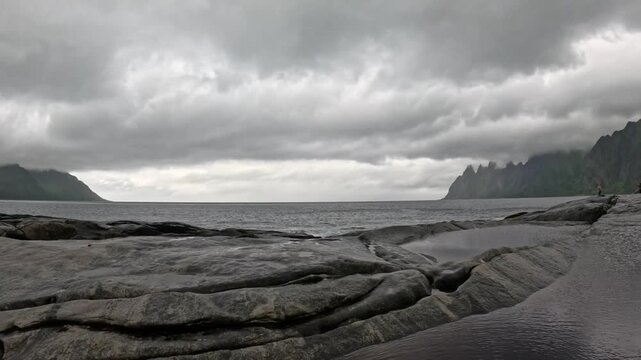 Static ultra wide view of Tungeneset granite rocks and tide pools with Okshornan peaks in Senja Norway