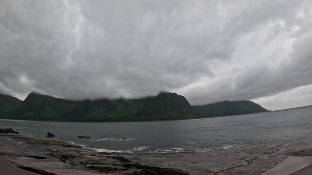 Static ultra wide view of low clouds over Ersfjord mountains from Tungeneset coast in Senja Norway