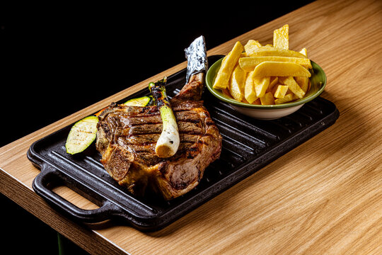 Grilled Tomahawk Ribeye Steak Served on Cast Iron Skillet with French Fries, Grilled Vegetables, and Scallion