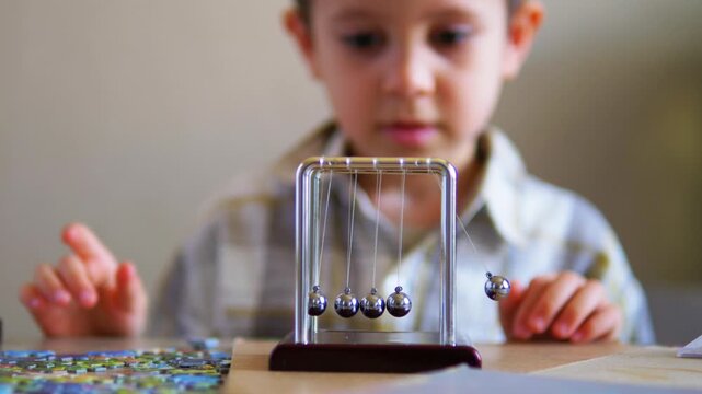 Curious boy carefully observing a stationary Newton's Cradle while learning about physics