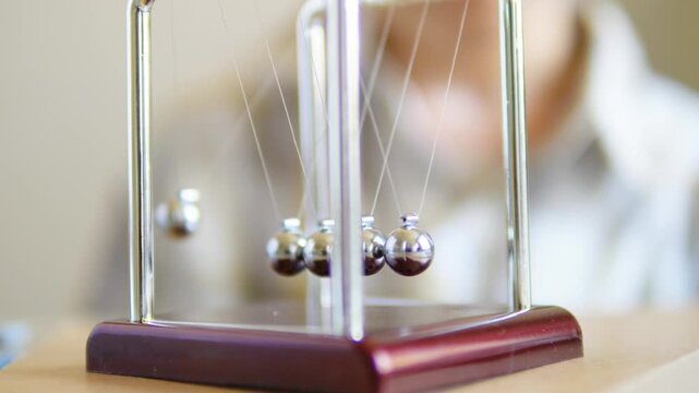 Hand releasing a metal sphere on a Newton's cradle to demonstrate physics and momentum
