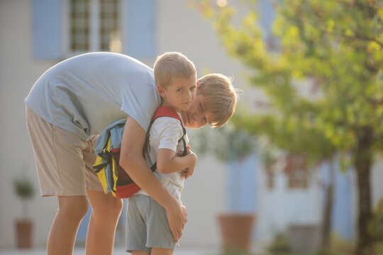Adult holding child carrying, in outdoor residential area, with backpack, building, from a side view perspective, with blue, white accents, and affectionate mood.