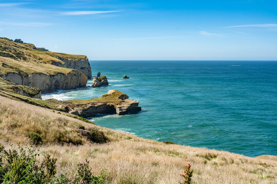 Sandsteinklippen und Felsformationen am Tunnel Beach mit tuerkisfarbenem Meer bei Dunedin Neuseeland