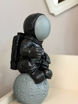 Decorative astronaut figurine sitting on a moon model in a modern interior, space exploration concept with copy space.