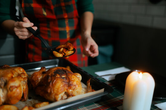 Housewife Serving Roasted Christmas Chicken With Baked Garlic Potatoes. Close up of woman using ladle to serve holiday dinner near candle