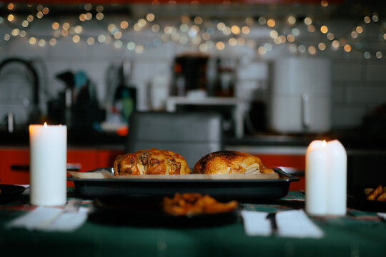 Roasted Christmas Chicken On Table With Blurred Festive Lights Background. Delicious holiday roast poultry on baking tray between two burning white candles