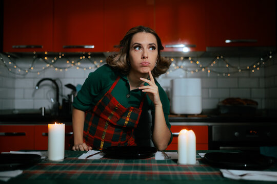 Thoughtful Housewife Sitting At Decorated Christmas Dinner Table Thinking
Pensive young woman with hand on chin looking away before holiday celebration