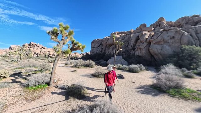 A mature couple walks together on rocky trails in Joshua Tree National Park during sunset. They enjoy their time outdoors.