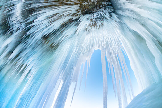 Ice cave with icicles in Baikal lake at sunset. Icicles on the rocks. Winter landscape of Baikal lake, Russia