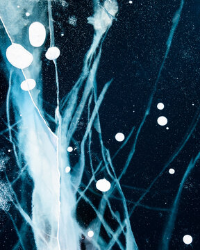 Transparent blue ice with cracks on Baikal lake in winter. Abstract winter nature background.