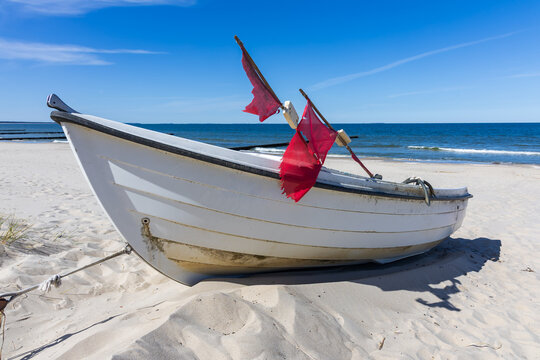 Small white fishing boat with red flags resting on sunny sandy beach