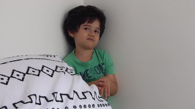 Sad and guilty young boy standing alone in the corner of a room looking down after being disciplined or scolded at home