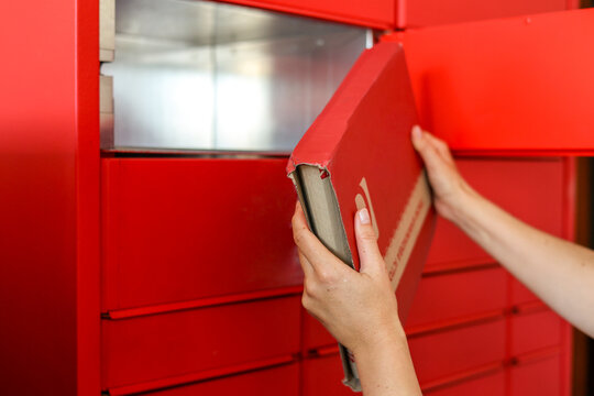 Automated package delivery locker for shipment and pickup of parcels and mail. Woman taking out cardboard box from parcel locker, closeup. Receiving and sending parcels in automated terminal concept.