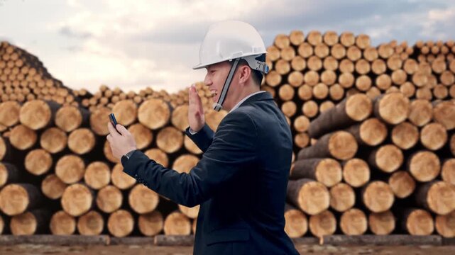 Side View of Asian Businessman Use Smartphone, Video Call While Walking with Stacked timber logs pile at outdoor lumber yard