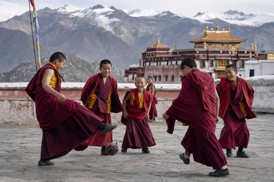 Tibetan Buddhist monks and boys playing soccer outside a Himalayan monastery. Joyful community life, cultural tradition, spirituality, and travel in a mountain landscape.